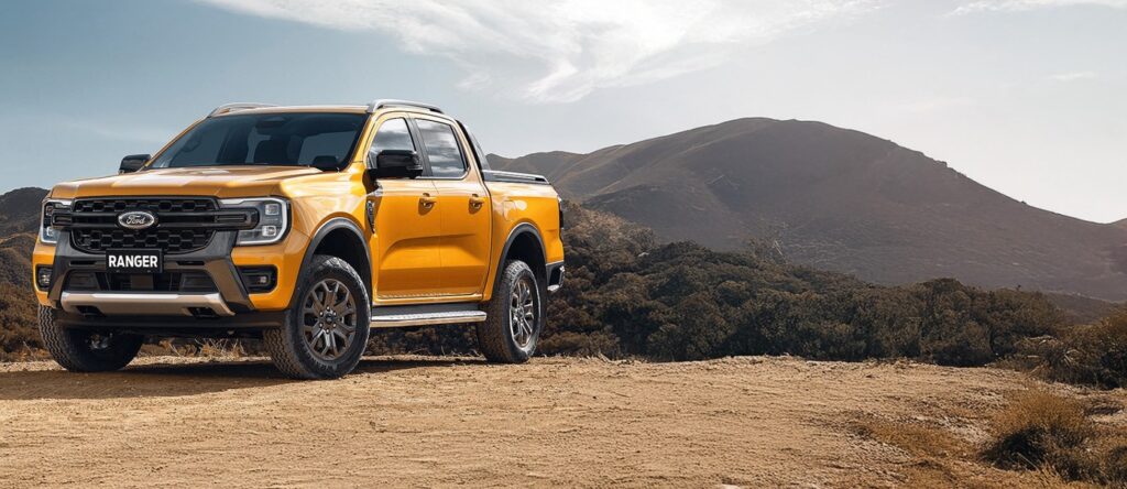 Yellow Ford Ranger pickup truck parked on dirt with mountain background.