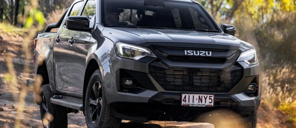 All-Terrain Isuzu D-Max pickup truck driving on a dirt road in a natural outdoor setting.