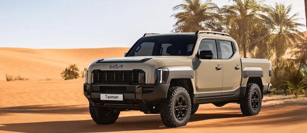 Kia Tasman off-road vehicle in desert landscape with palm trees, rugged and durable design.
