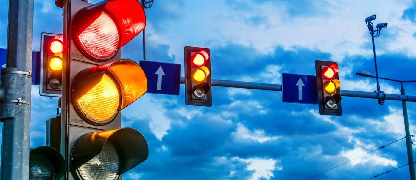 Traffic lights showing red and yellow signals against a cloudy sky.