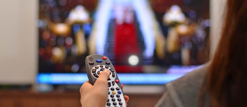 Remote control pointed at a television screen showing a movie or TV show.