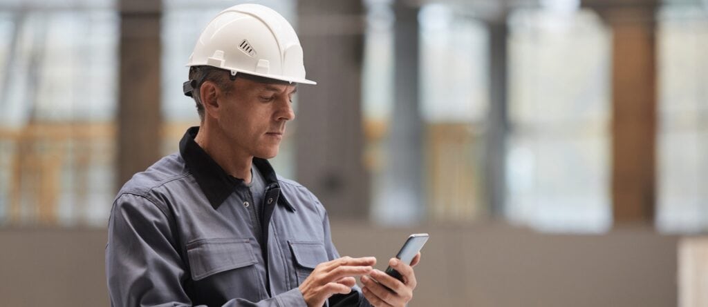 High-voltage electrical technician inspecting equipment with a smartphone in a modern industrial set.