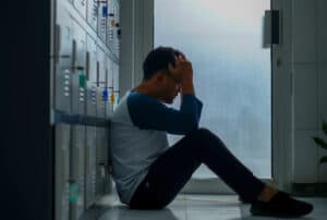 young man sitting against lockers with knees up and hands to his head