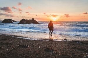 individual walking on beach towards water and sunset