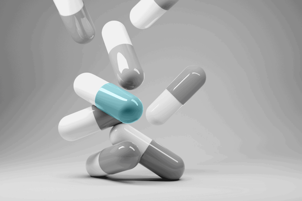 multiple grey and white pill capsules with one white and blue capsule