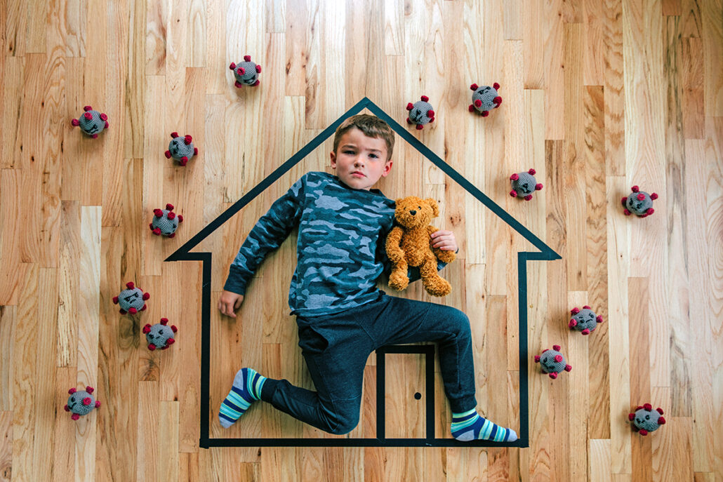 little boy lying inside tape outline of home with covid virus surrounding him