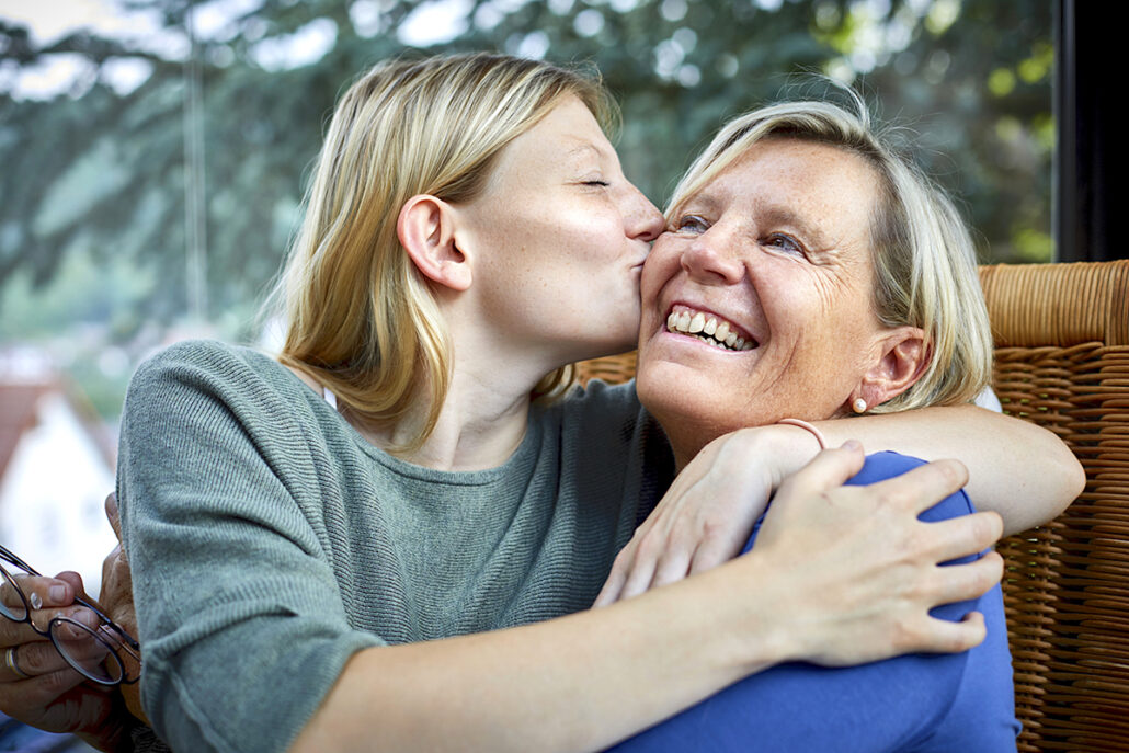 Happy older woman and young woman hugging and kissing in armchair