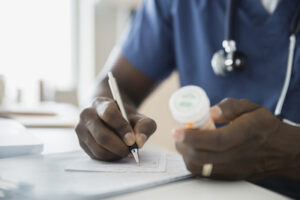 doctor writing prescription holding pill bottle