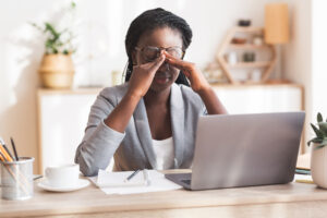 girl sitting at desk looking at computer with hands in between eyes