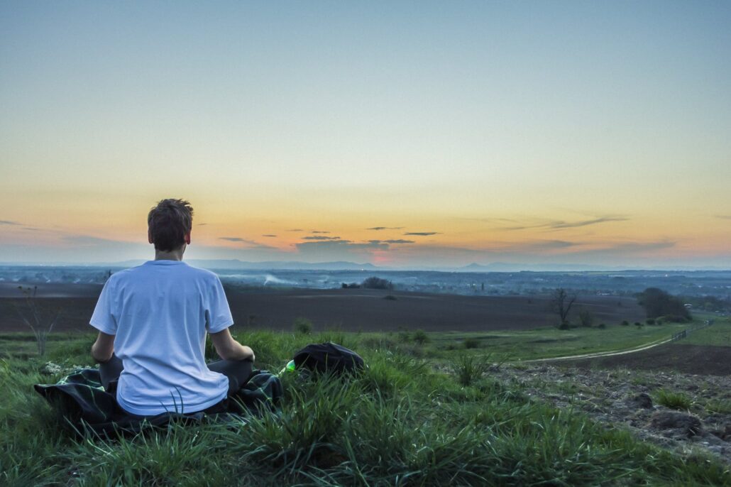 man meditating facing sun going down