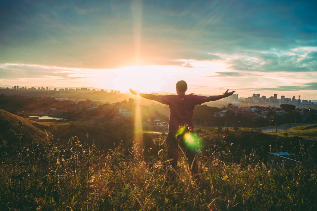 man standing facing sun with arms out