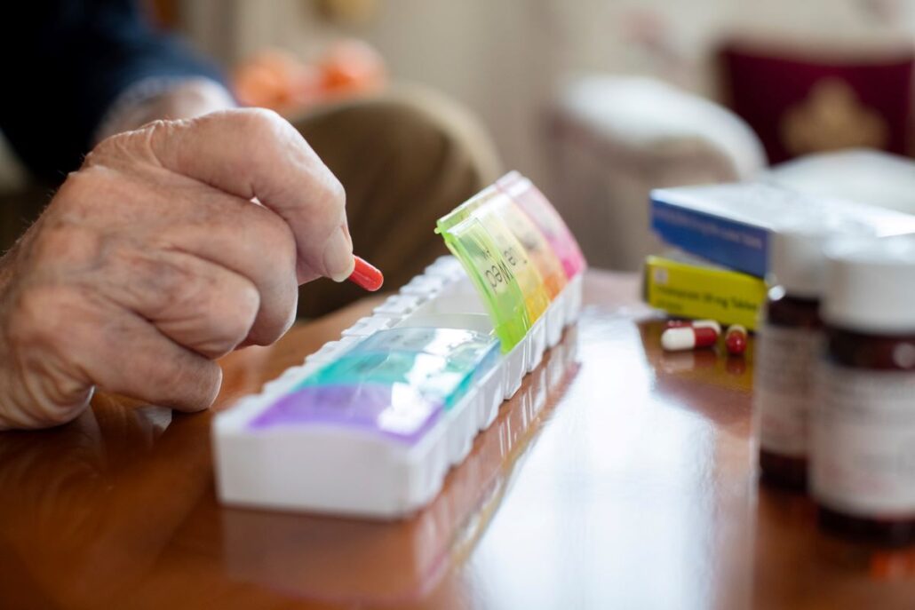 man putting pill capsule in rainbow pill container