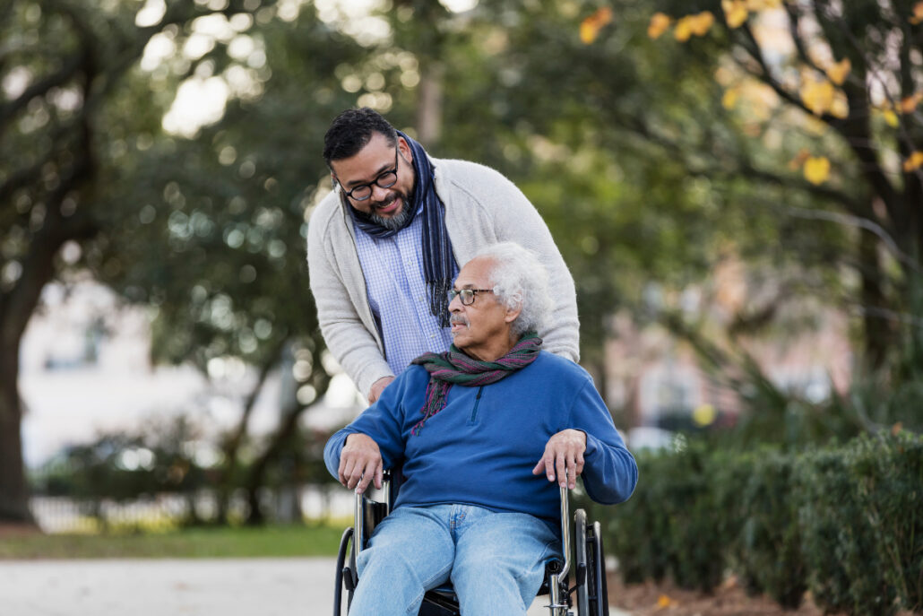 adult male pushing older adult male in wheelchair in park