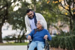 adult male pushing older adult male in wheelchair in park