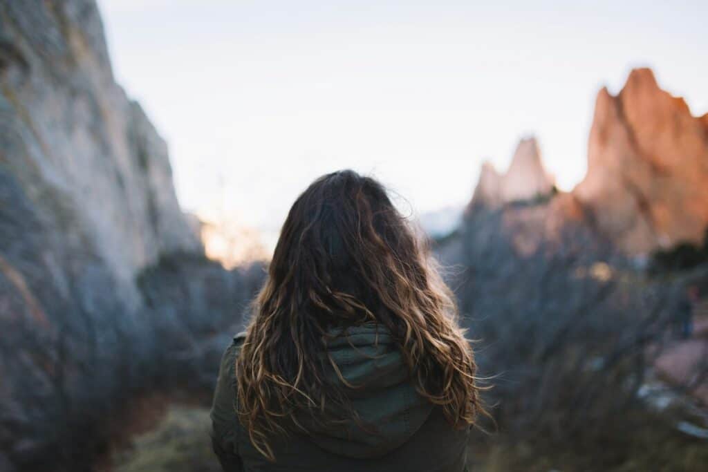 Bakifrån syns en kvinna som står och betraktar bergstoppar, en visuell representation av mindfulness och att vara fullt närvarande.