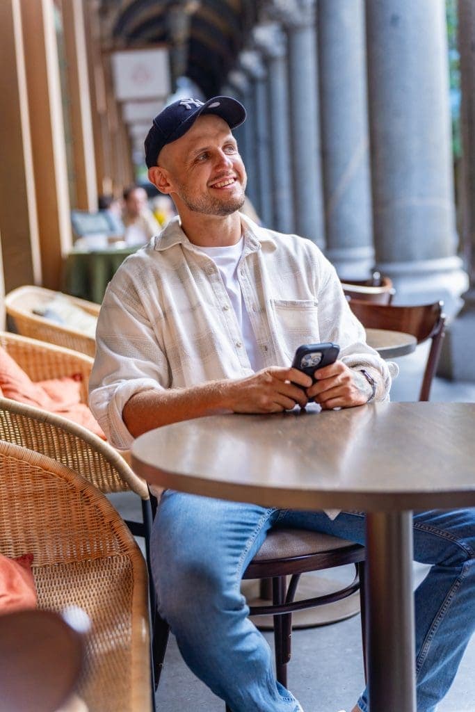 Relaxed-Dating-Photos-Sydney-NSW – Professional Photographer Sydney Ext: Young bald man in a white shirt sitting at a cafe table having his dating photo taken by dating photographer Georgie Green in Sydney NSW Image used in Frequently Asked Questions Section