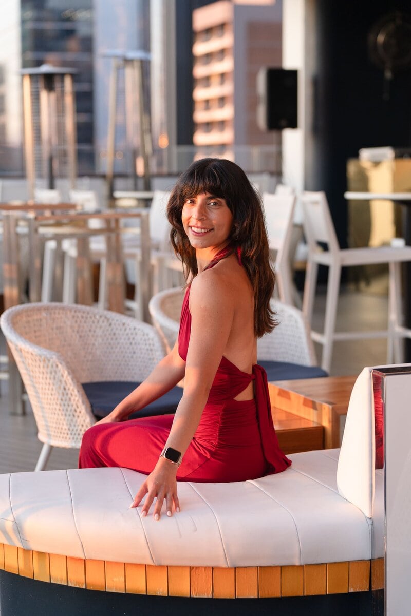 Indian Yoga Teacher wearing red and sitting in a roof top bar having her personal branding portrait taken by professional photographer Georgie Greene