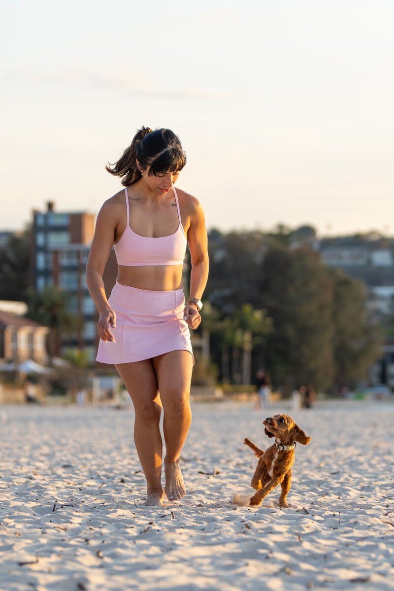 Indian Yoga Teacher wearing pink and walking her dog on the beach having her personal branding photo taken by Sydney Personal branding photographer Georgie Greene