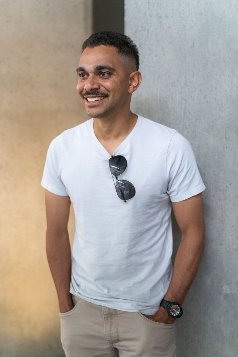 Young dark haired man wearing a white t-shirt and standing by a concrete wall having his dating photo taken by Sydney dating photographer Georgie Greene