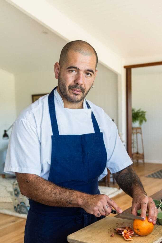 private chef in a blue apron cutting an orange and having his personal branding portrait taken by Sydney professional photographer Georgie Greene