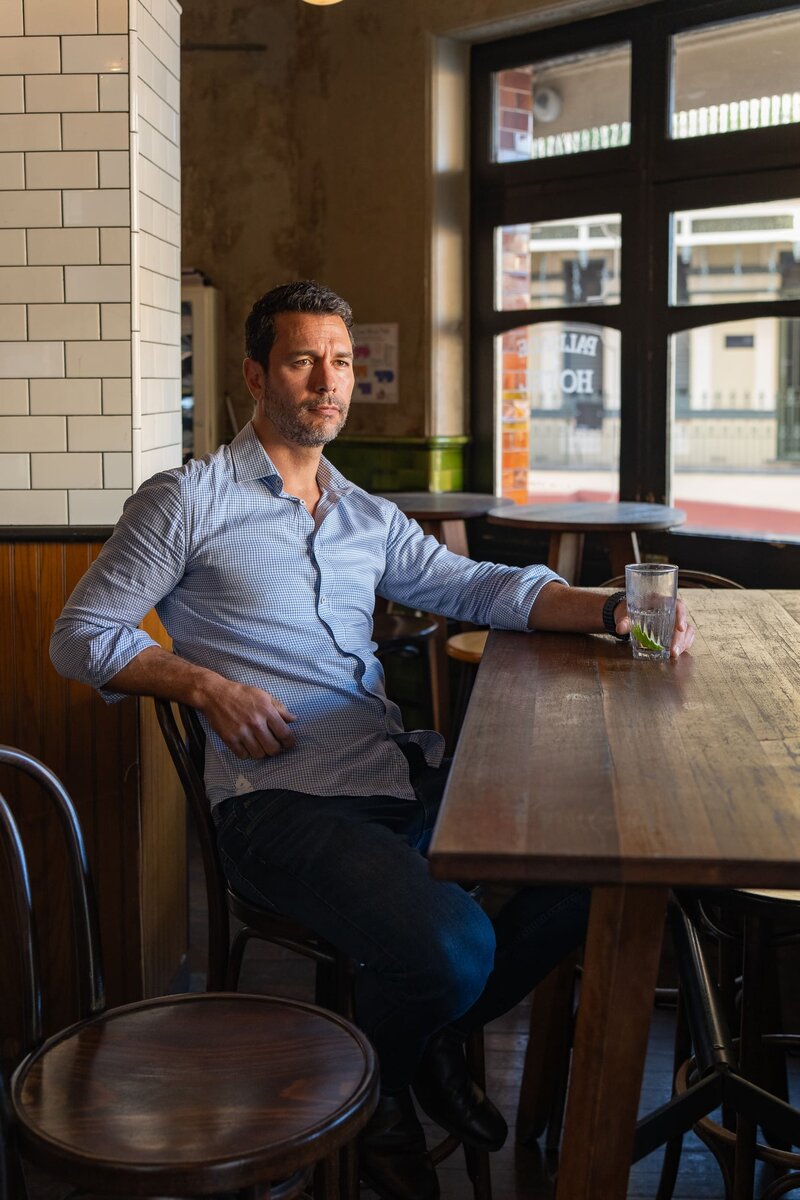 Dark hair man with beard wearing a blue shirt and sitting in a pub having his dating photo taken by top Sydney dating photographer Georgie