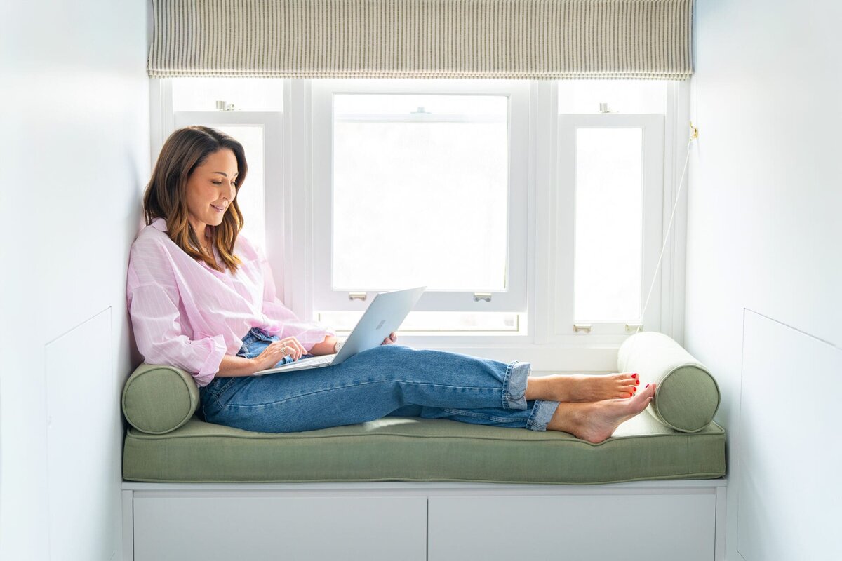 dark haired marketing specialist sitting on a green window seat typing at her computer having her personal branding photo taken by professional Sydney photographer Georgie Greene