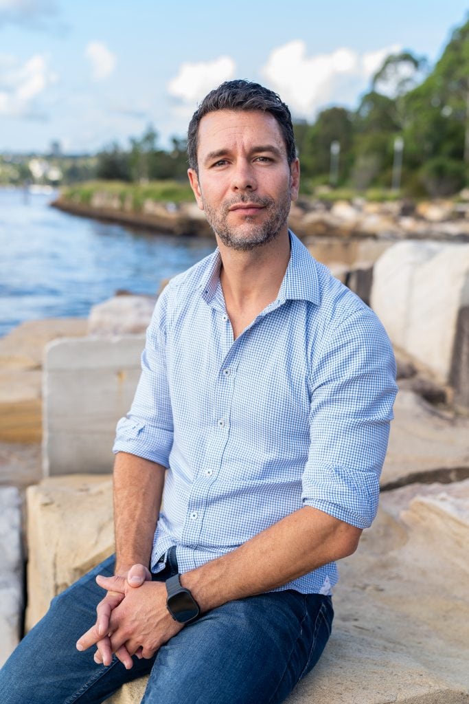 Sydney-Dating-Photography-Sydney-NSW – Professional Photographer Sydney Dark hair man with beard wearing a blue shirt and sitting by the water having his dating photo taken by top Sydney dating