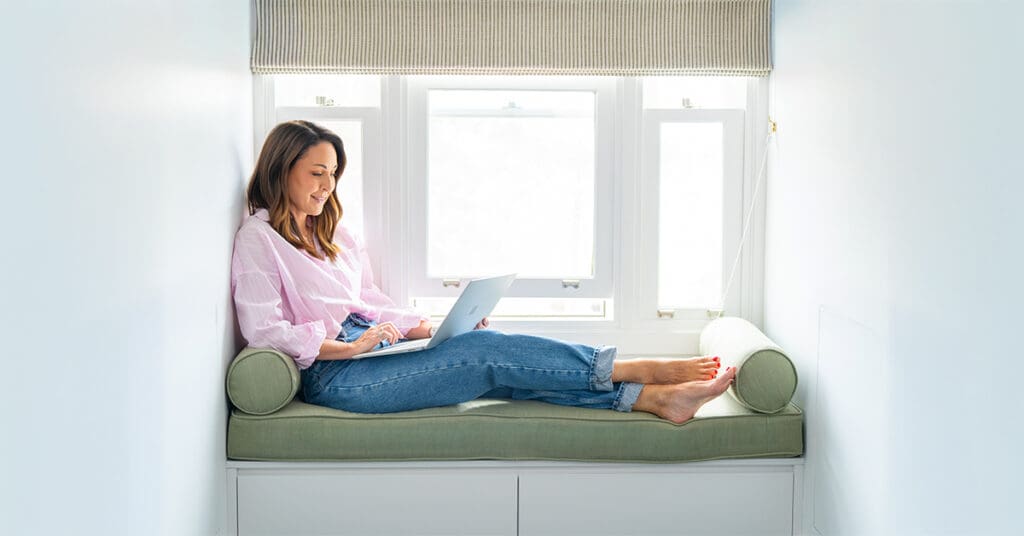 Sydney-Personal-Branding-Feature-Photo – Professional Photographer Sydney dark haired marketing specialist sitting on a green window seat typing at her computer having her personal branding photo taken by professional Sydney photographer Georgie Greene