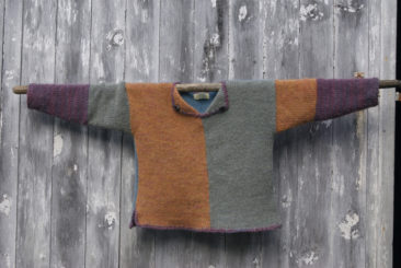 Vibrant color-blocked wool sweater displayed on a wooden pole against a rustic wooden wall. Perfect for cozy knitwear enthusiasts and lovers of handcrafted wool garments.