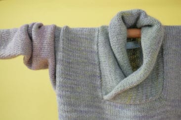 Soft pastel-colored wool sweater hanging on a wooden hanger, showcasing Seacolors Yarnery sustainable yarns and knitwear craftsmanship. Perfect for eco-friendly fashion and handmade wool clothing enthusiasts.