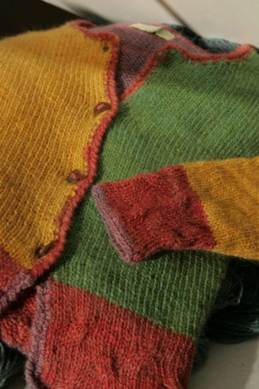 Nostalgic woven patchwork sweater made from colorful wool yarns, vibrant green, yellow, and red tones, showcasing handmade artisanal craftsmanship and cozy textured knitting, perfect for fall and winter wear.