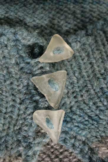 Seacolors yarnery sea glass buttons on cozy gray knitted fabric, eco-friendly jewelry accessory, handmade sea glass craft, sustainable fashion, ocean-inspired embellishment.