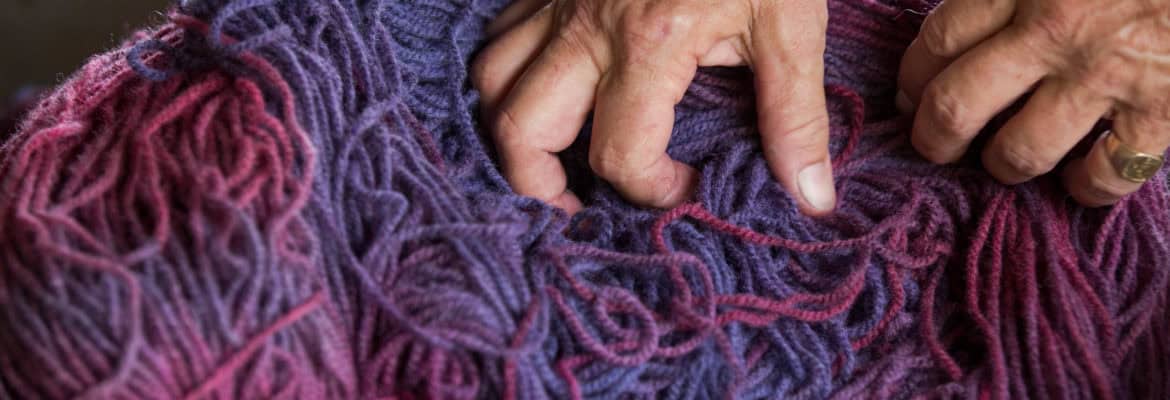 Vivid purple and pink wool yarn being handwoven with hands, showcasing Seacolors Yarnery's vibrant, high-quality fiber art craft. Ideal for knitting and crochet projects.