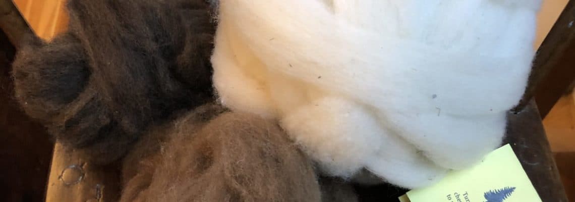 Soft white and brown wool roving and felted wool accessories on a rustic wooden chair, showcasing high-quality wool fibers for felting and craft projects. Perfect for knitting, felting, or fiber art enthusiasts.