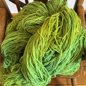 Vibrant lime green SeaColors Yarnery yarn skeins, showcasing soft, chunky, hand-dyed wool yarn perfect for knitting and crochet projects, displayed on a rustic wooden chair.