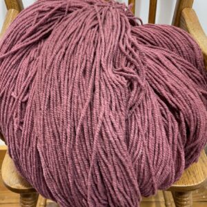Soft pink chunky yarn for knitting, crocheting, and craft projects on a wooden chair. Perfect for cozy blankets, sweaters, and home decor using high-quality, vibrant wool yarn.