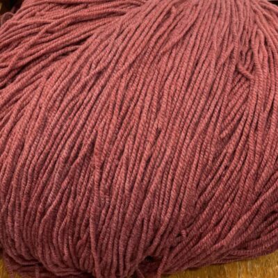 Soft pink yarn from SeaColors Yarnery, perfect for knitting or crocheting cozy handmade projects, displayed on a wooden chair.