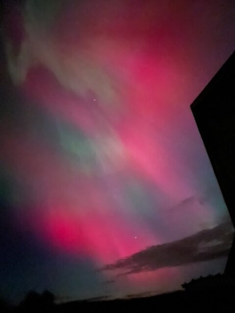 Vibrant northern lights display with pink, green, and purple hues over a dark landscape, showcasing stunning natural sky colors ideal for nature and astronomy enthusiasts.