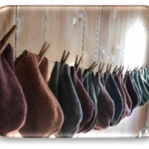 Soft wool yarns in earthy tones hanging on wooden pegs, showcasing Seacolors Yarnery collection for cozy knitting and crochet projects, emphasizing quality, variety, and sustainable materials.