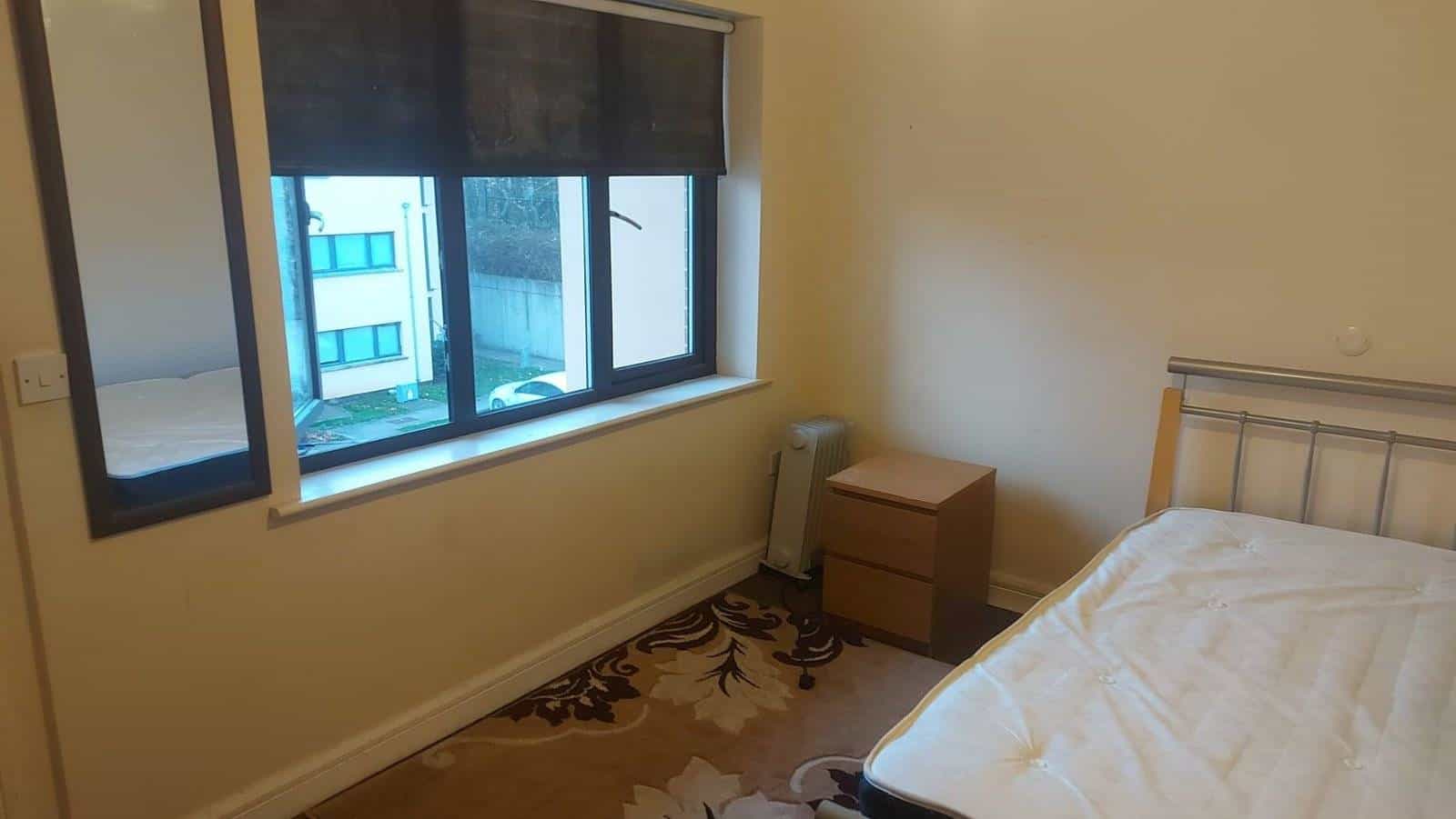 Double room with ensuite in Dublin 22 featuring a bed, window, bedside table and patterned rug. – Ghar.ie property listing