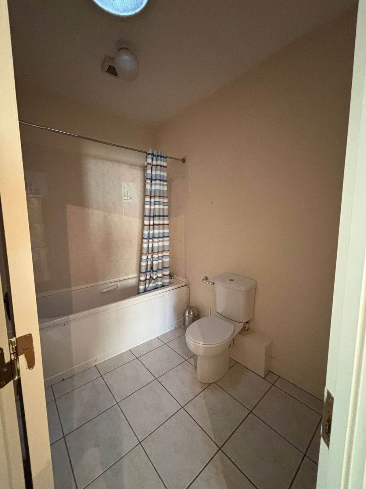 Bathroom with a white toilet, tub with shower curtain, and tile flooring in Mullingar. – Ghar.ie property listing