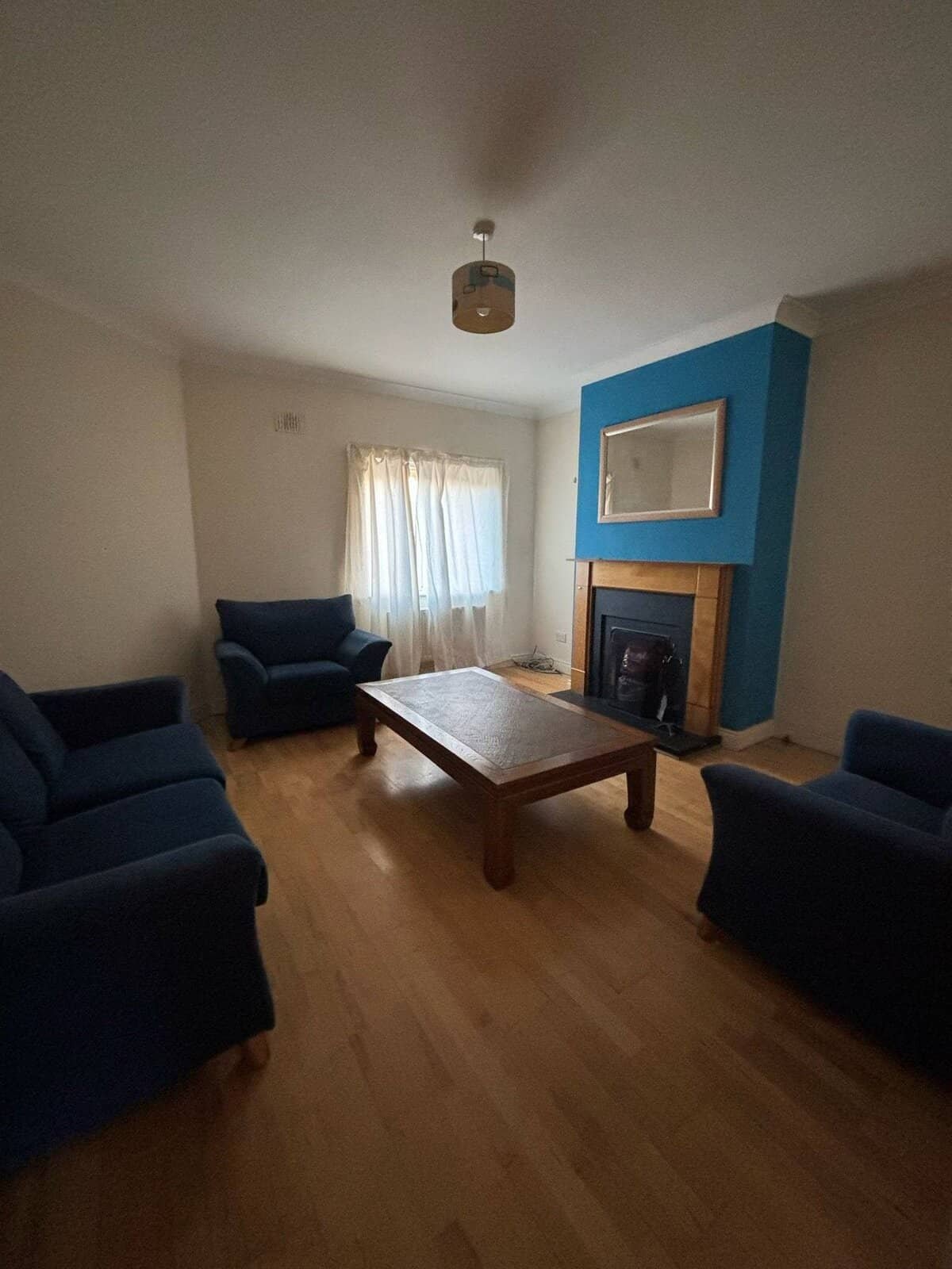Mullingar living room with blue sofas, wooden floor, fireplace, and natural light from a window. – Ghar.ie property listing