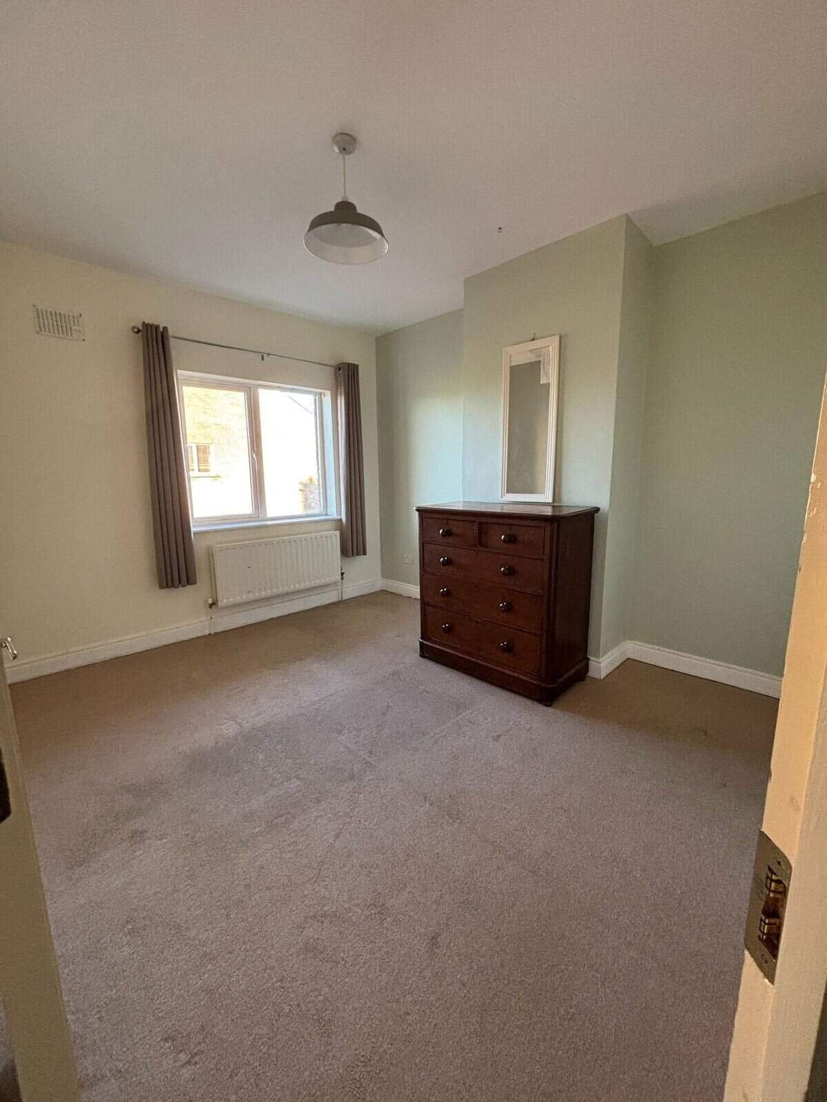 Bright bedroom in a Mullingar 3 bed property featuring a window and wooden dresser. – Ghar.ie property listing