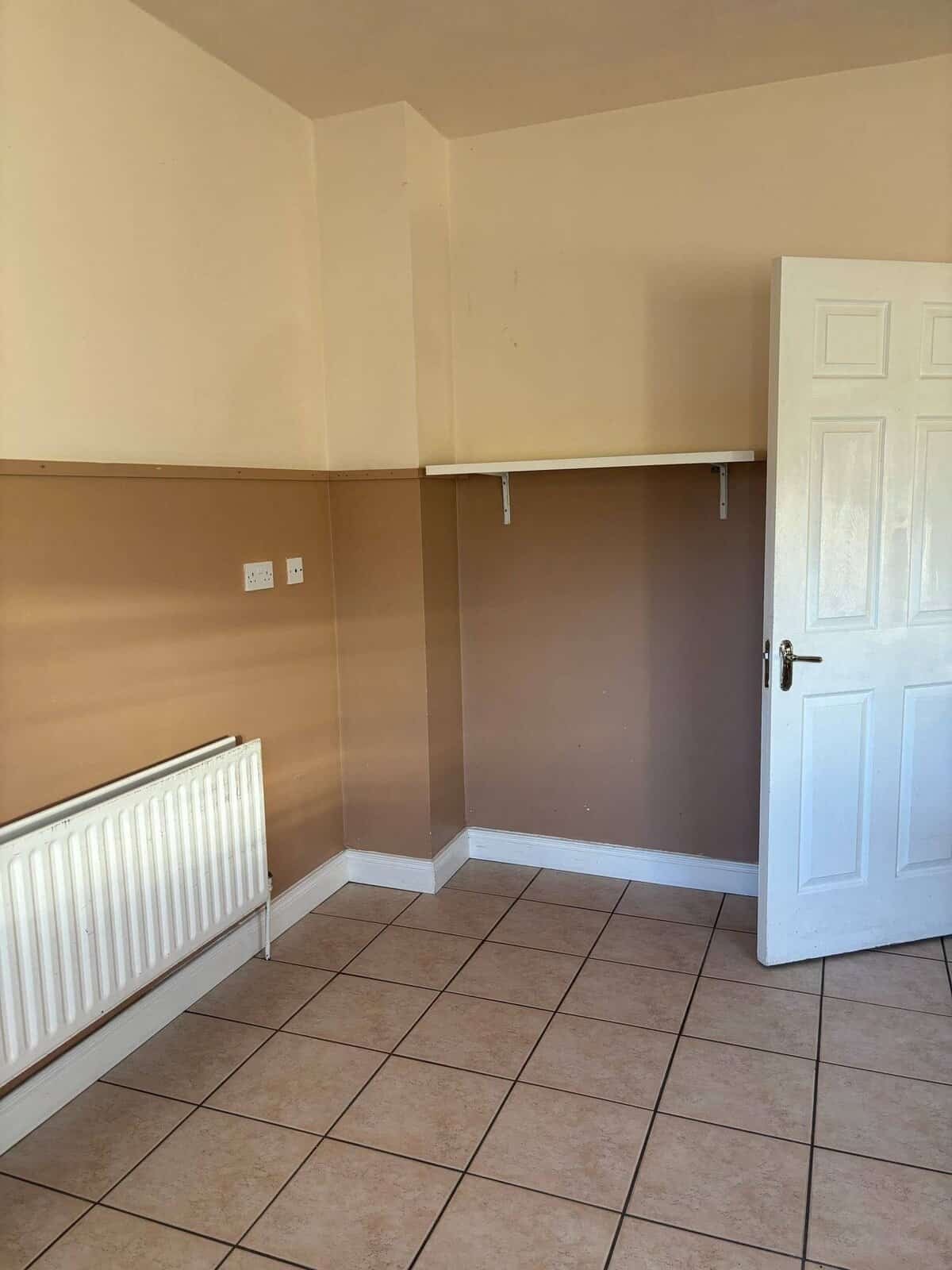 Mullingar bright bedroom with neutral walls, tiled floor, radiator, and white door and shelf. – Ghar.ie property listing