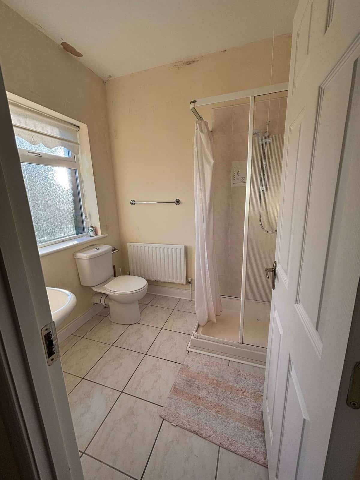 Bathroom with toilet, sink, shower, tile floor, and window in a Mullingar 3 bed property. – Ghar.ie property listing