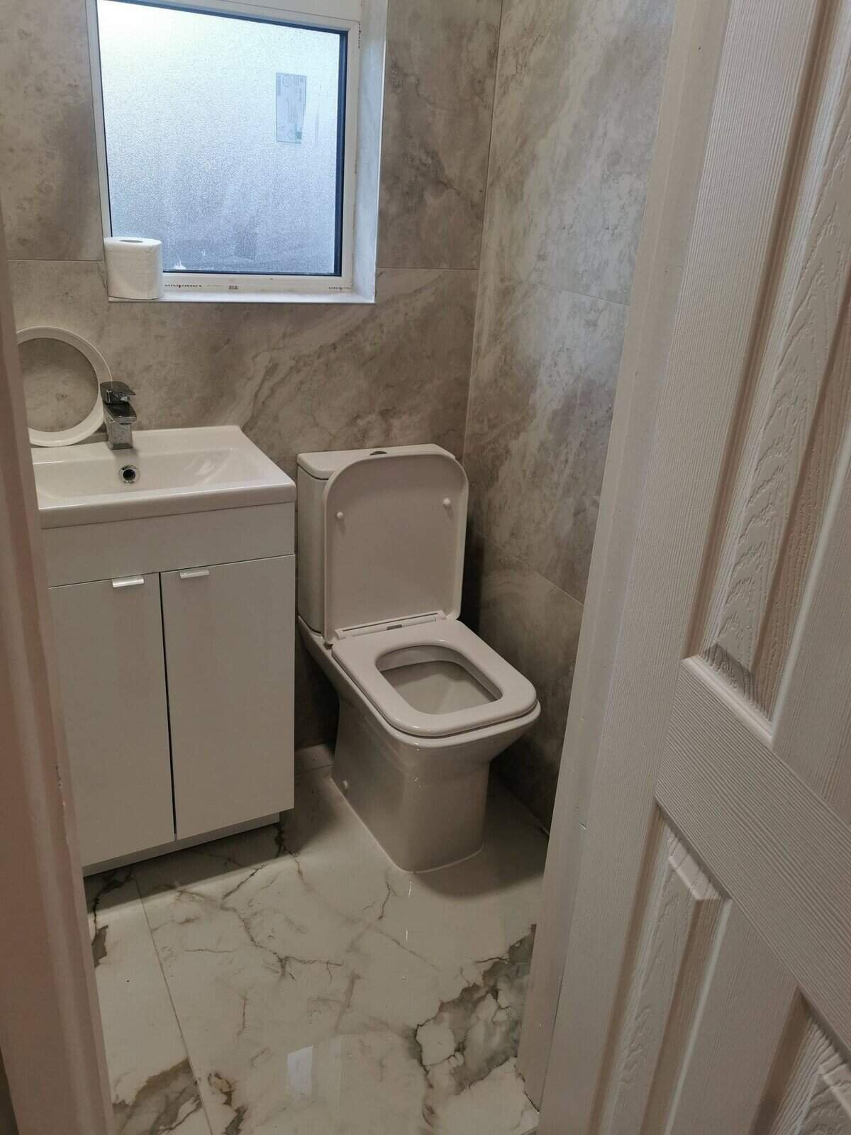 Modern bathroom with toilet, sink, cabinet, marble floor, and window in a one bedroom apartment. – Ghar.ie property listing