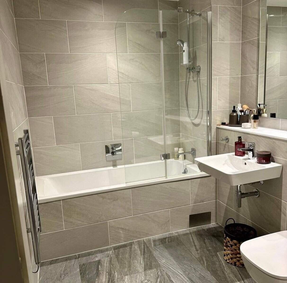 Modern bathroom with gray tile, bathtub with glass screen, sink, and heated towel rack. – Ghar.ie property listing