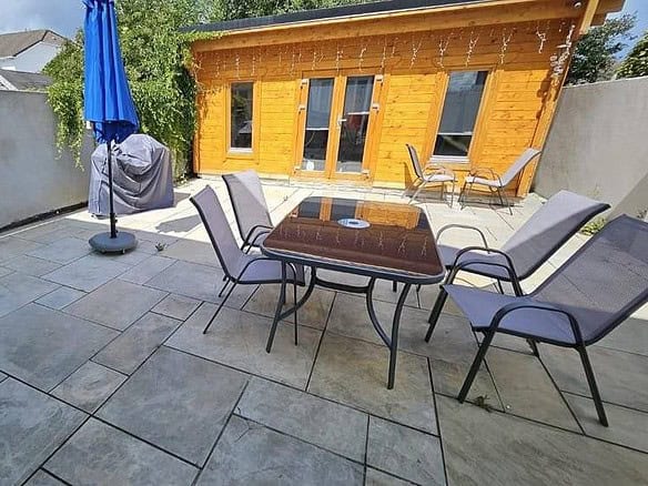 Outdoor patio area with table, chairs, and a blue umbrella, Dublin 13. Log cabin in background. – Ghar.ie property listing