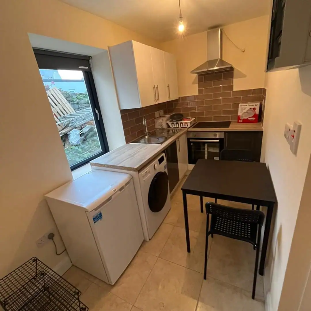 Compact kitchen in a Phibsborough flat for rent, featuring a washing machine, dining table and modern appliances. – Ghar.ie property listing