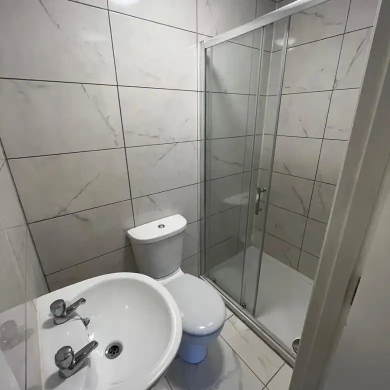 Bathroom with white marble effect tiles, toilet, sink, and glass shower in Dublin 7 flat. – Ghar.ie property listing